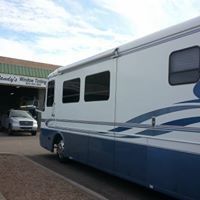 A large white and blue rv is parked in front of a garage.