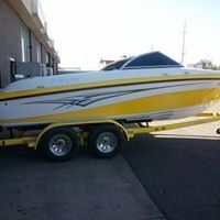 A yellow and white boat is on a trailer parked in front of a building.