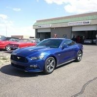 A blue mustang is parked in front of a car dealership.