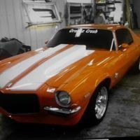An orange and white muscle car is parked in a garage.