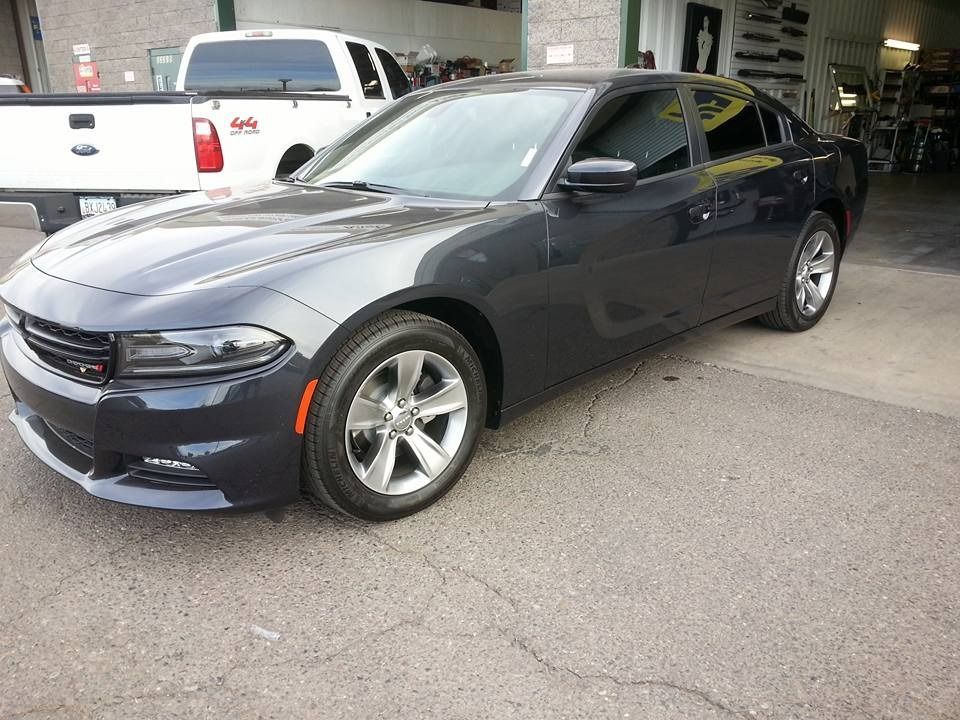 A black dodge charger is parked in a garage next to a white truck.