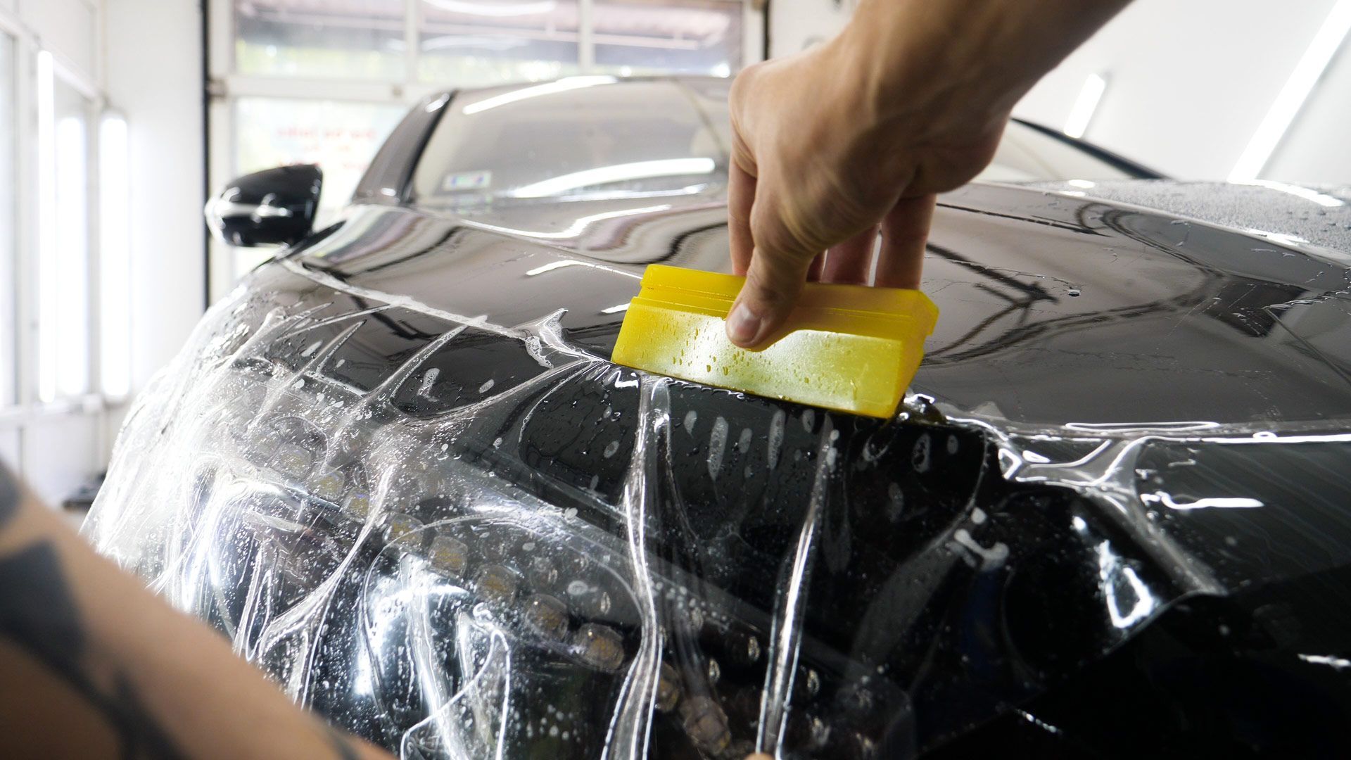 A person is applying a protective film to the hood of a car.