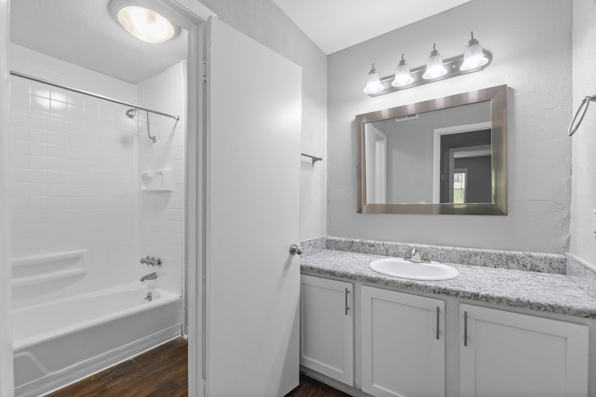A bathroom with a white vanity, granite countertop, rectangular mirror, light fixture, and a tub-shower combo.