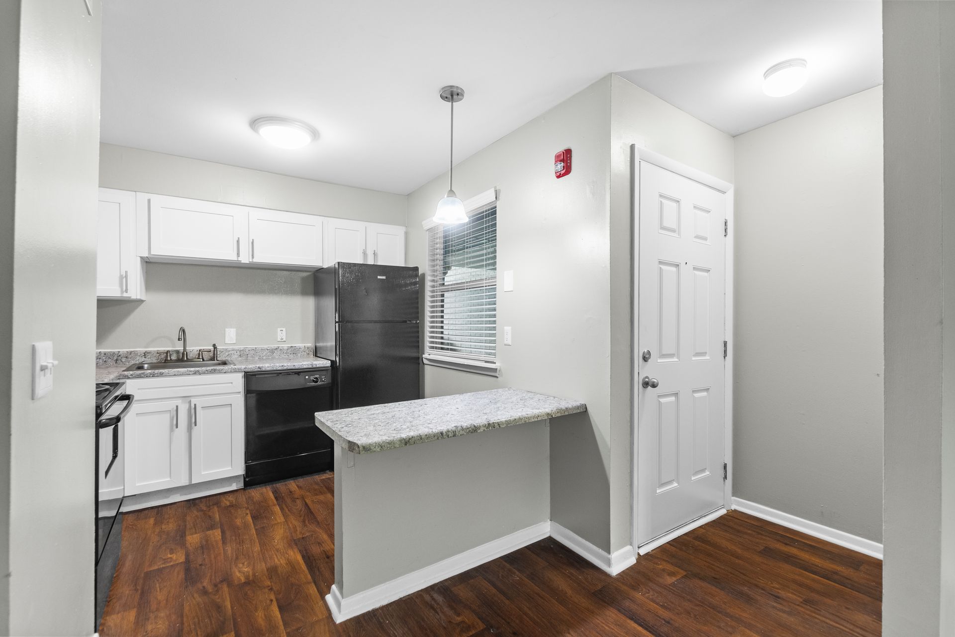 A bright kitchen with white cabinets, dark countertops and appliances, a breakfast bar, and wood-style flooring.