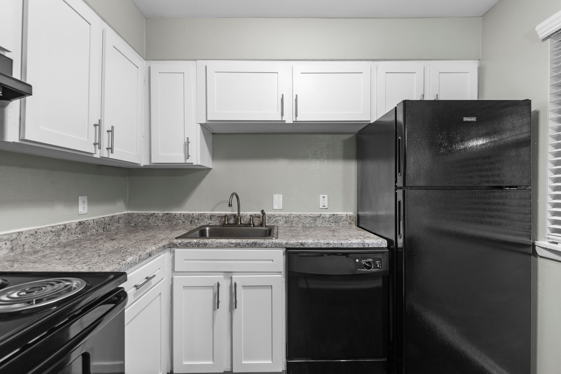 A kitchen with white cabinets, granite countertops, a stainless steel sink, and black appliances.