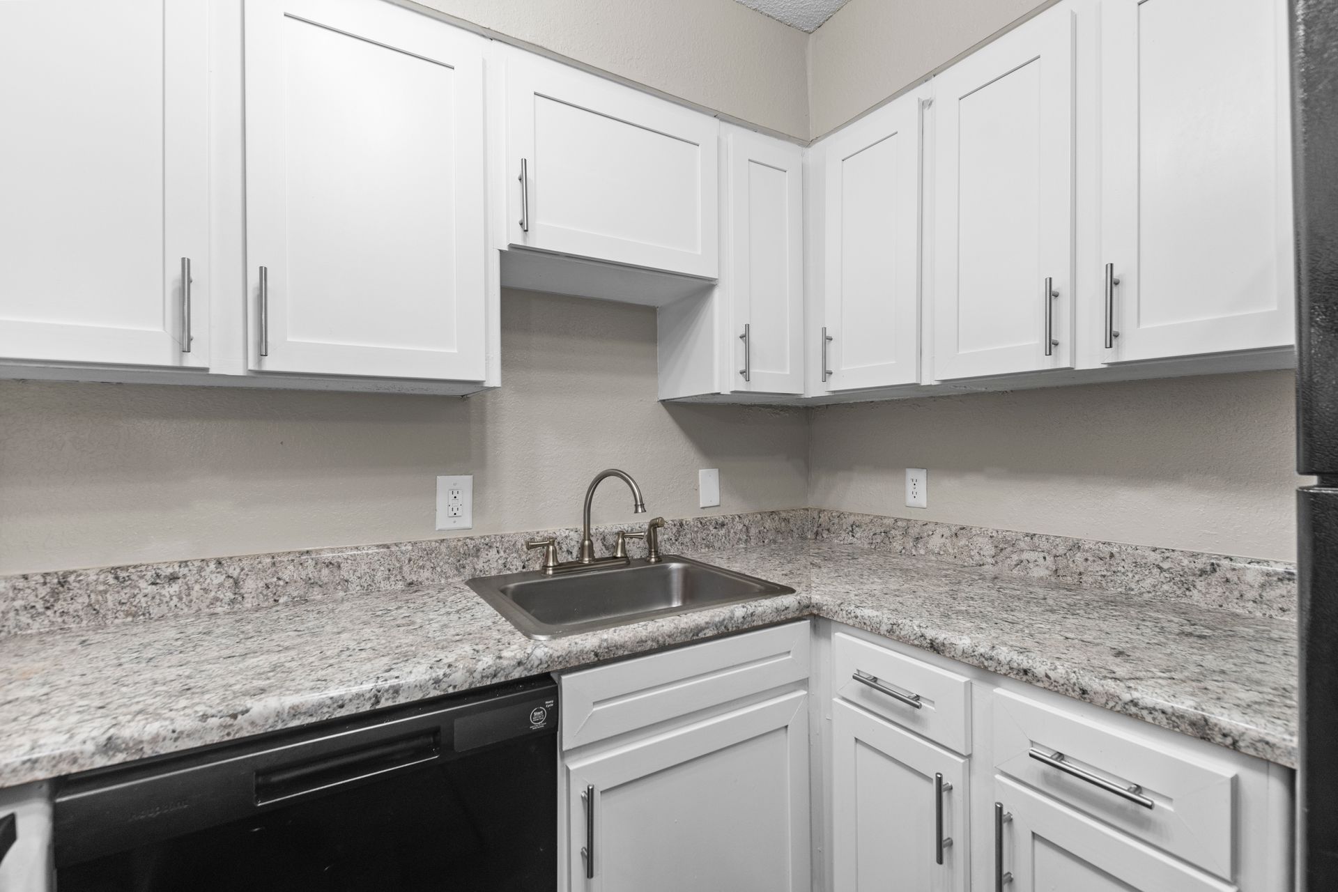 A kitchen featuring white cabinets, granite countertops, a stainless steel sink, and black appliances.