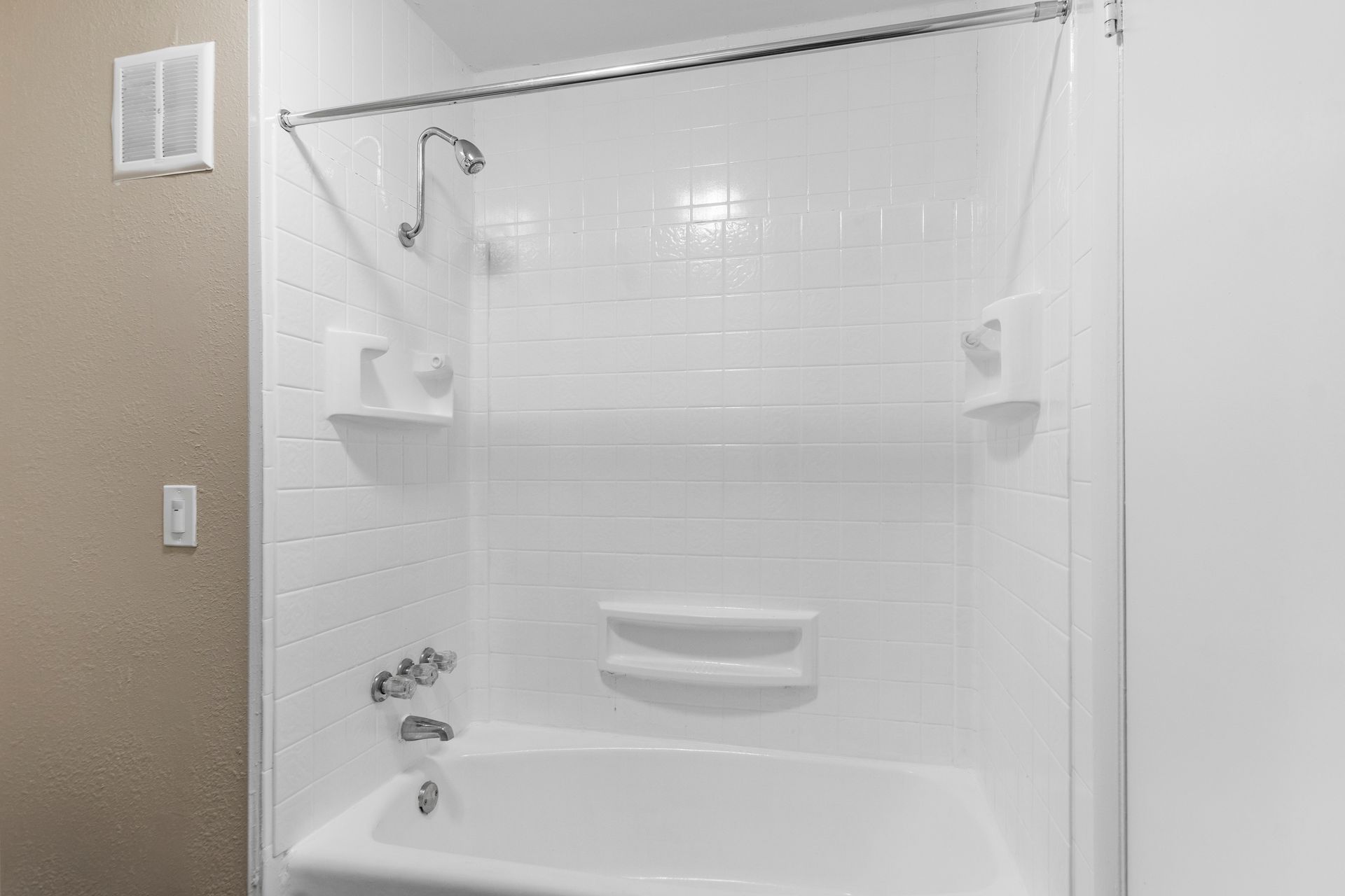 A white bathtub and shower surround with white subway tile pattern, including a shower head, faucet, and soap niches.