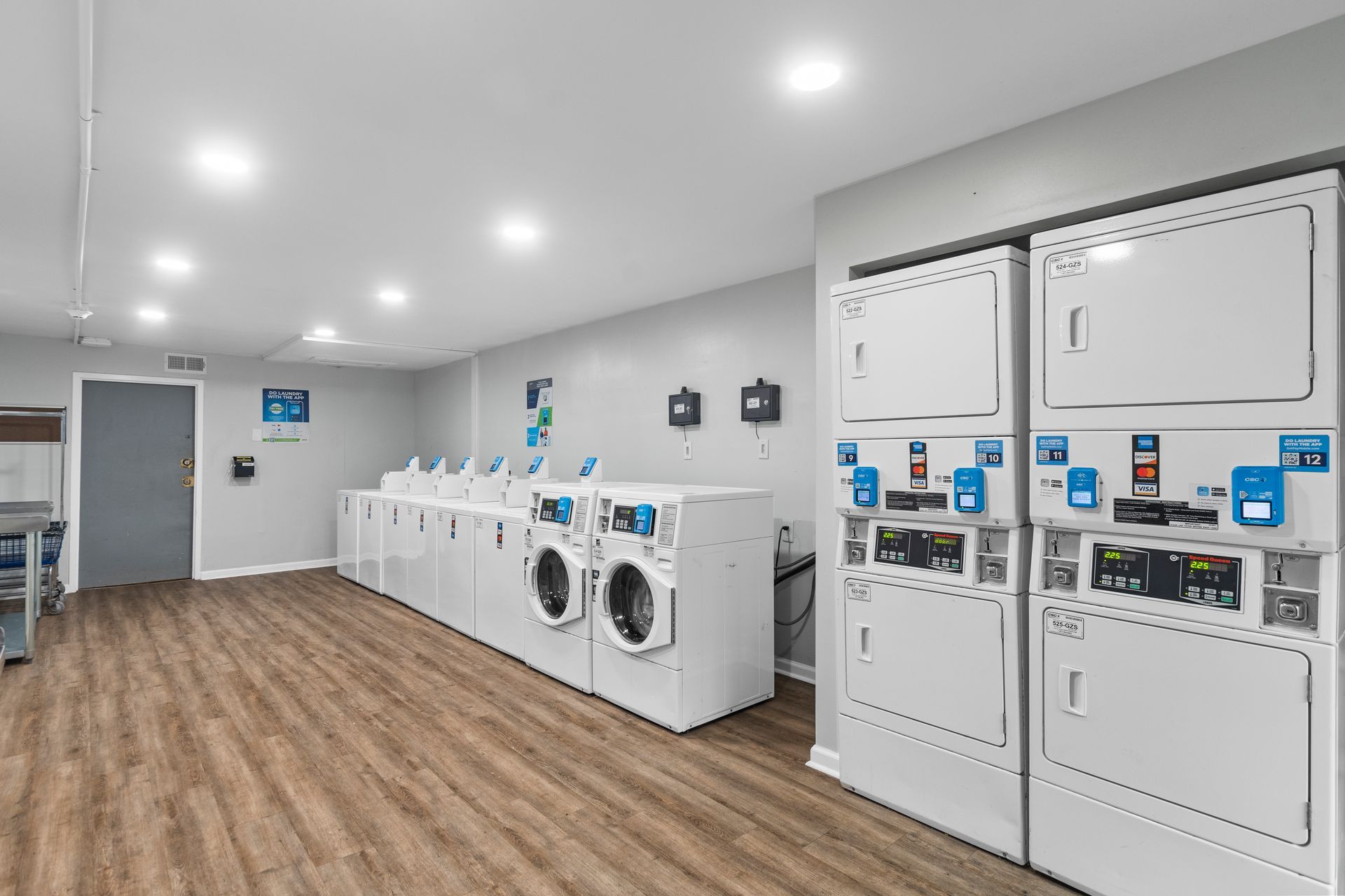 A bright, modern laundry room with white washer and dryer units lined up along a light grey wall over wood-look flooring.