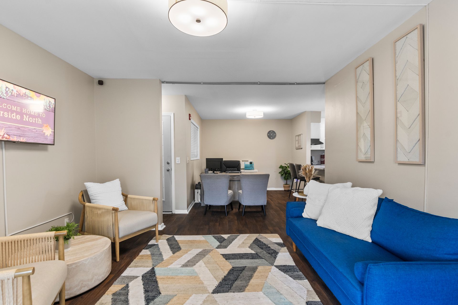 A modern office waiting area featuring a blue sofa, a tan armchair, a geometric rug, and a desk in the background.