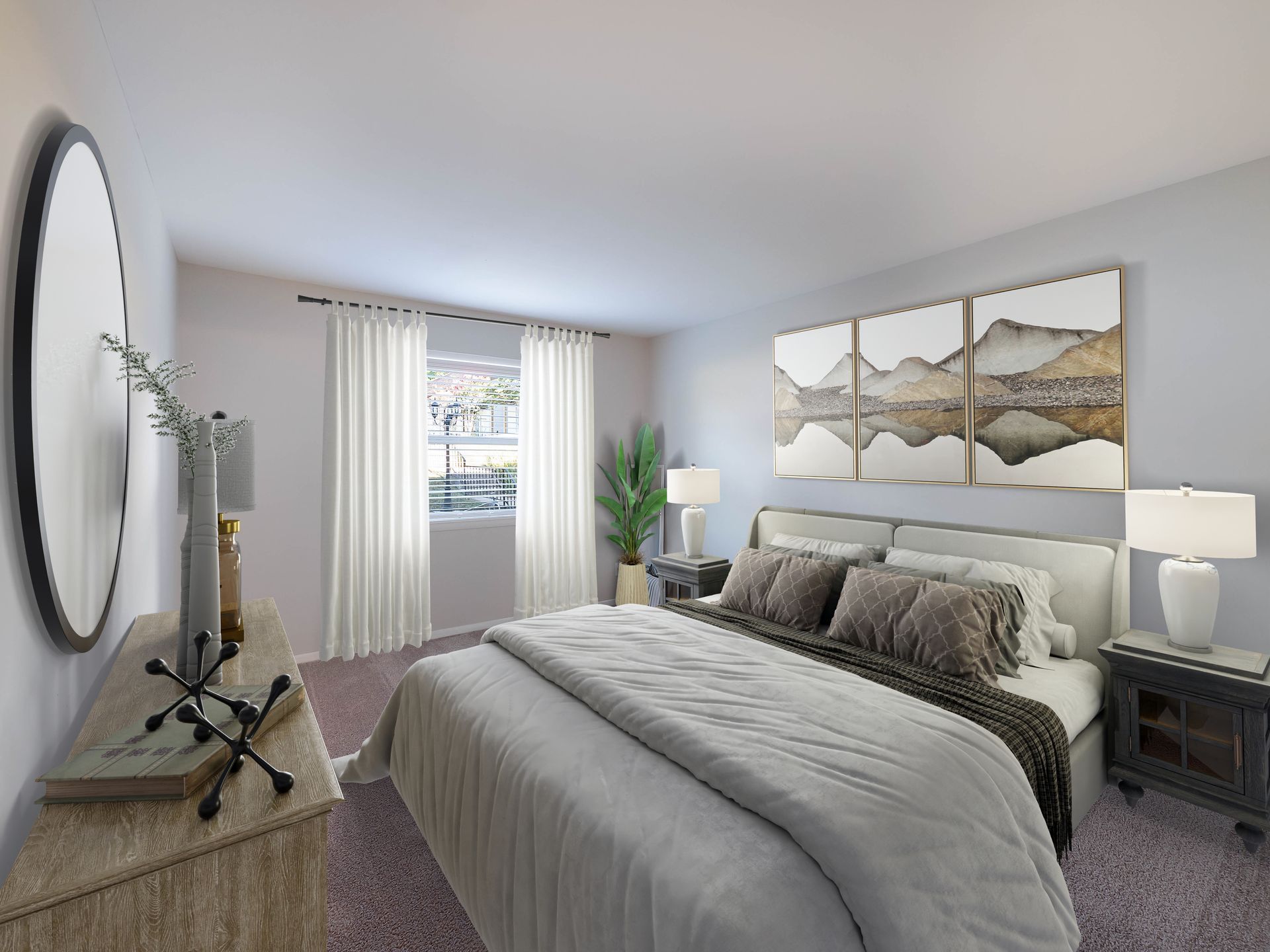 A bright bedroom with a queen bed, neutral bedding, a wall-mounted landscape triptych, a side table, and a round mirror.