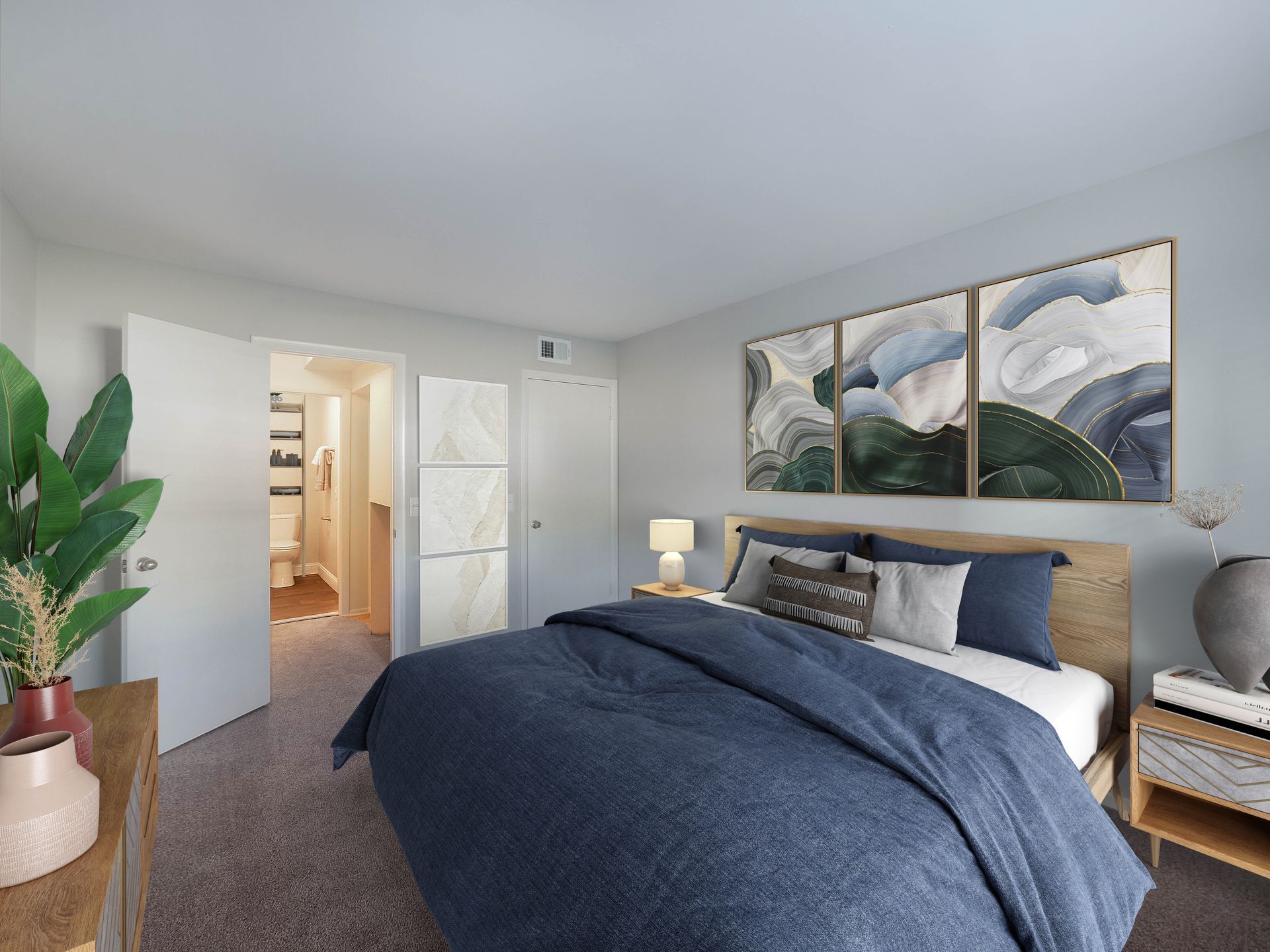 A bedroom with a queen bed featuring a navy duvet, three framed abstract art pieces above the headboard, and an open door.