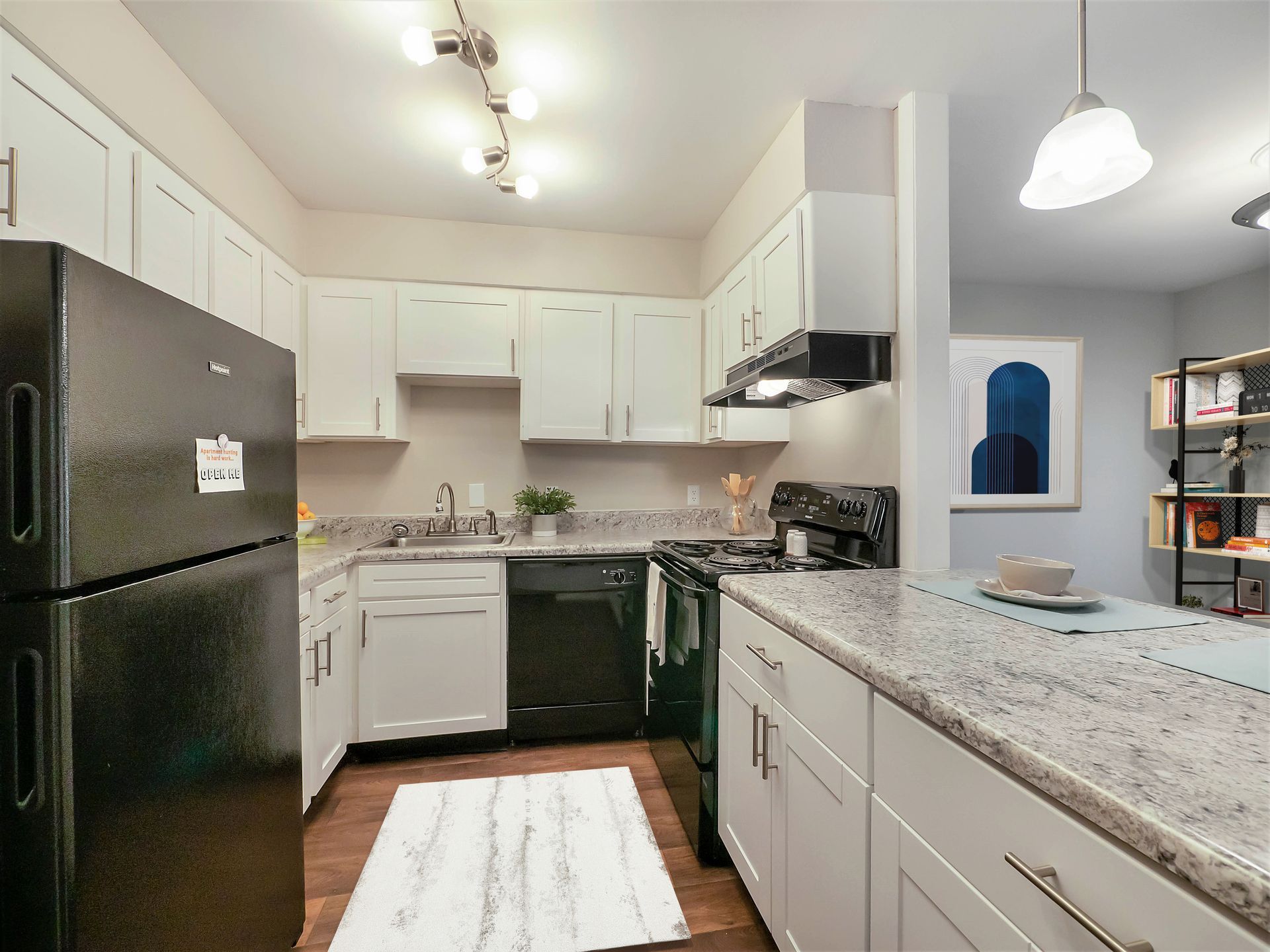 Modern kitchen with white cabinets, speckled granite countertops, a black refrigerator, and an open dining area.