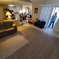 Living room with beige carpet, two sofas, a person opening a sliding door to the outside.