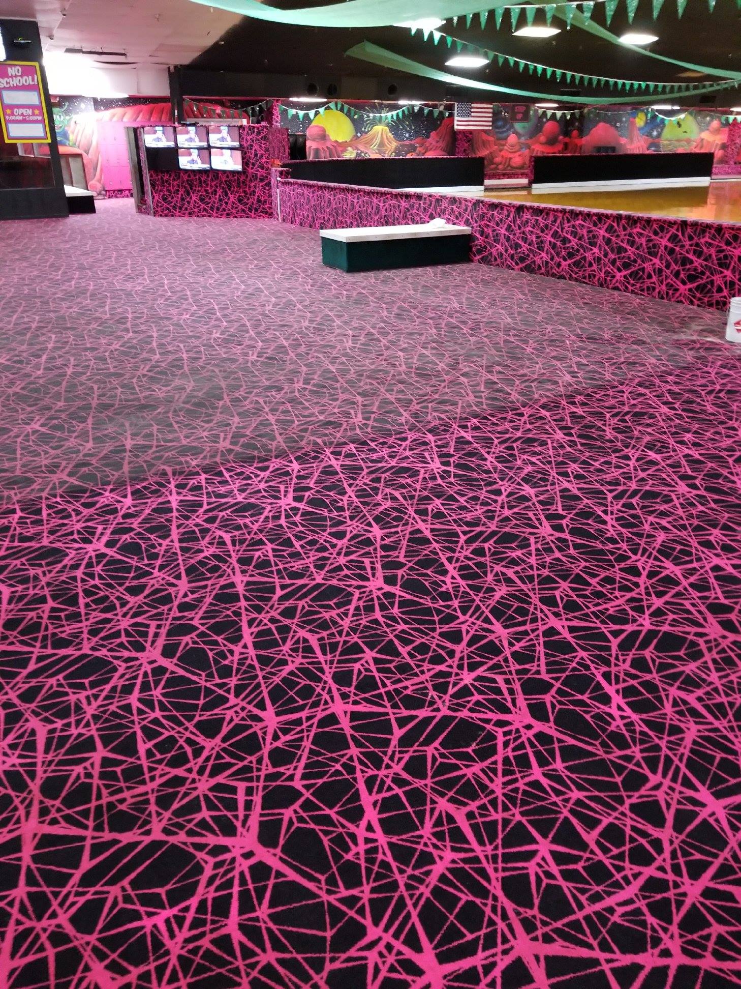 Pink and black patterned carpet in an indoor roller rink setting, a table and seating are visible.