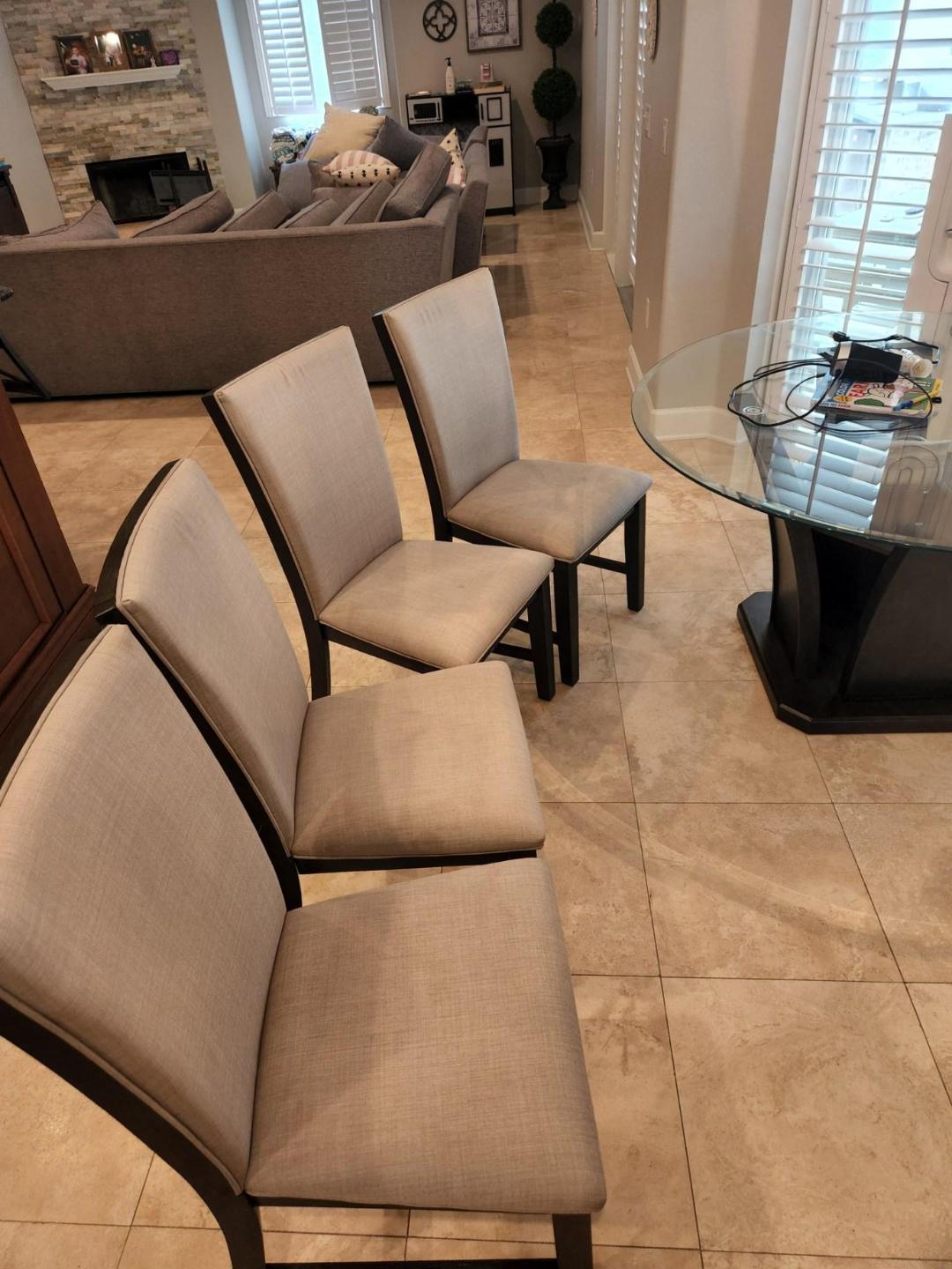 Four beige upholstered dining chairs with dark wood frames in a bright room.