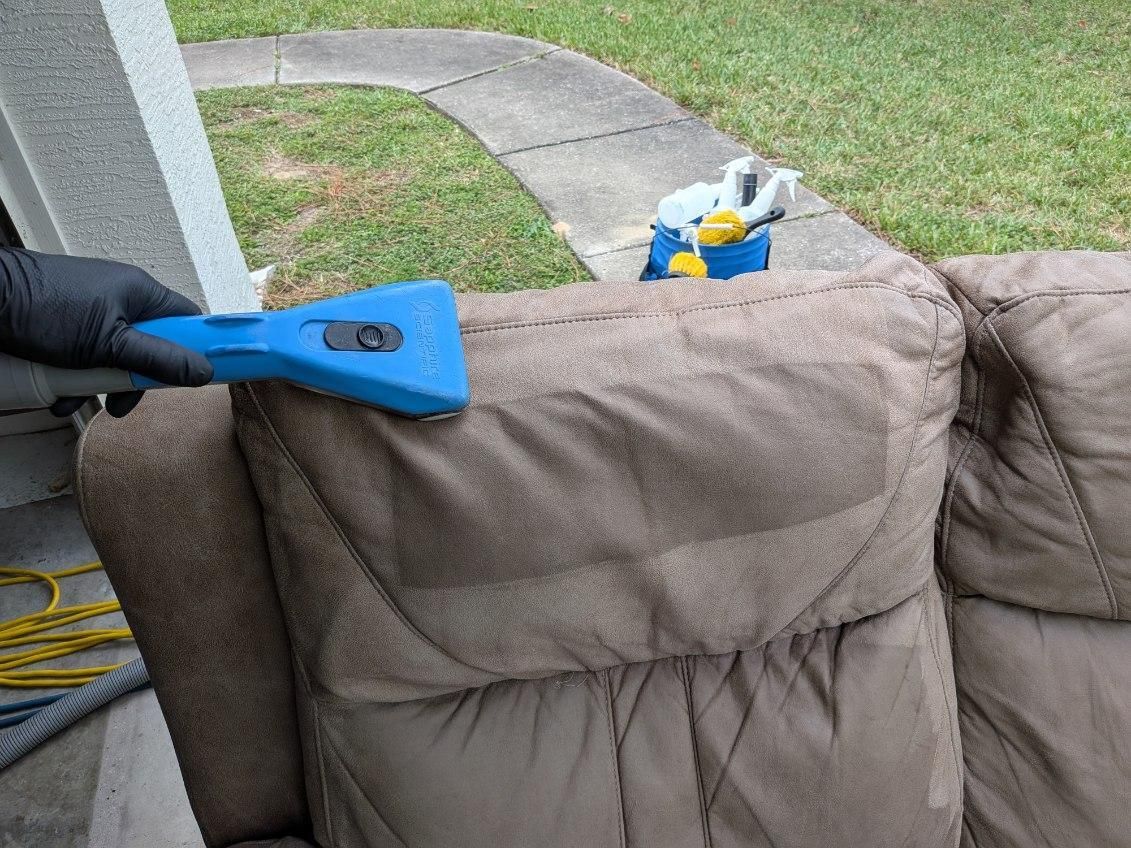 Person cleaning a tan couch with a blue upholstery cleaner outdoors.