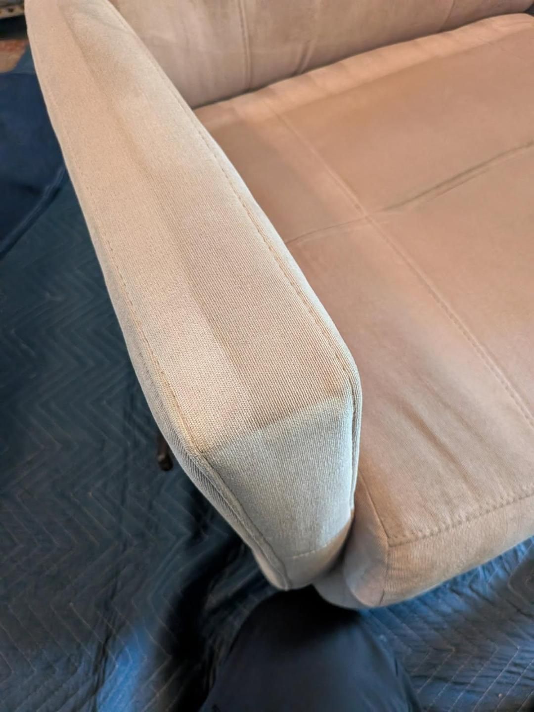 Close-up of a beige upholstered chair arm, with visible stitched fabric.