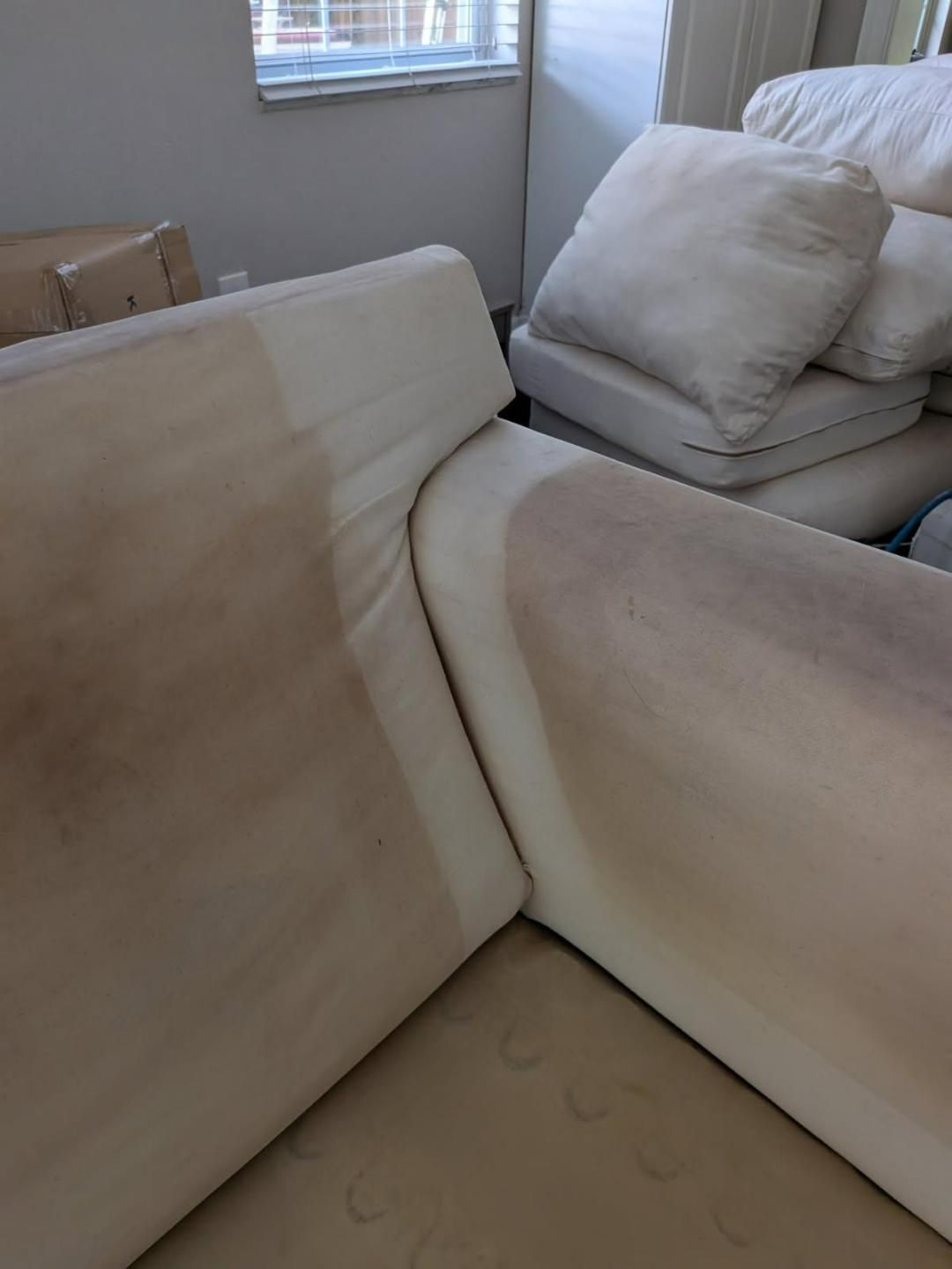 Beige sectional sofa with significant dark staining, possibly from use or spills.