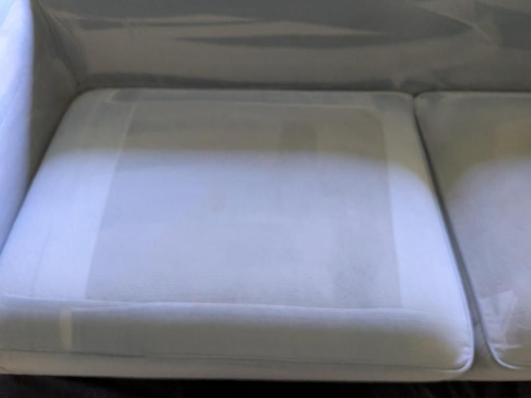 Close-up of a white sofa seat, covered in clear plastic for protection.