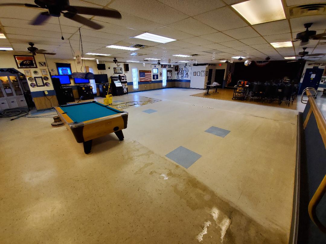 A large, empty rec room with a pool table, bar, and stage; some water on the floor.