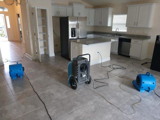 Kitchen with white cabinets and island, three blue air movers drying the floor.