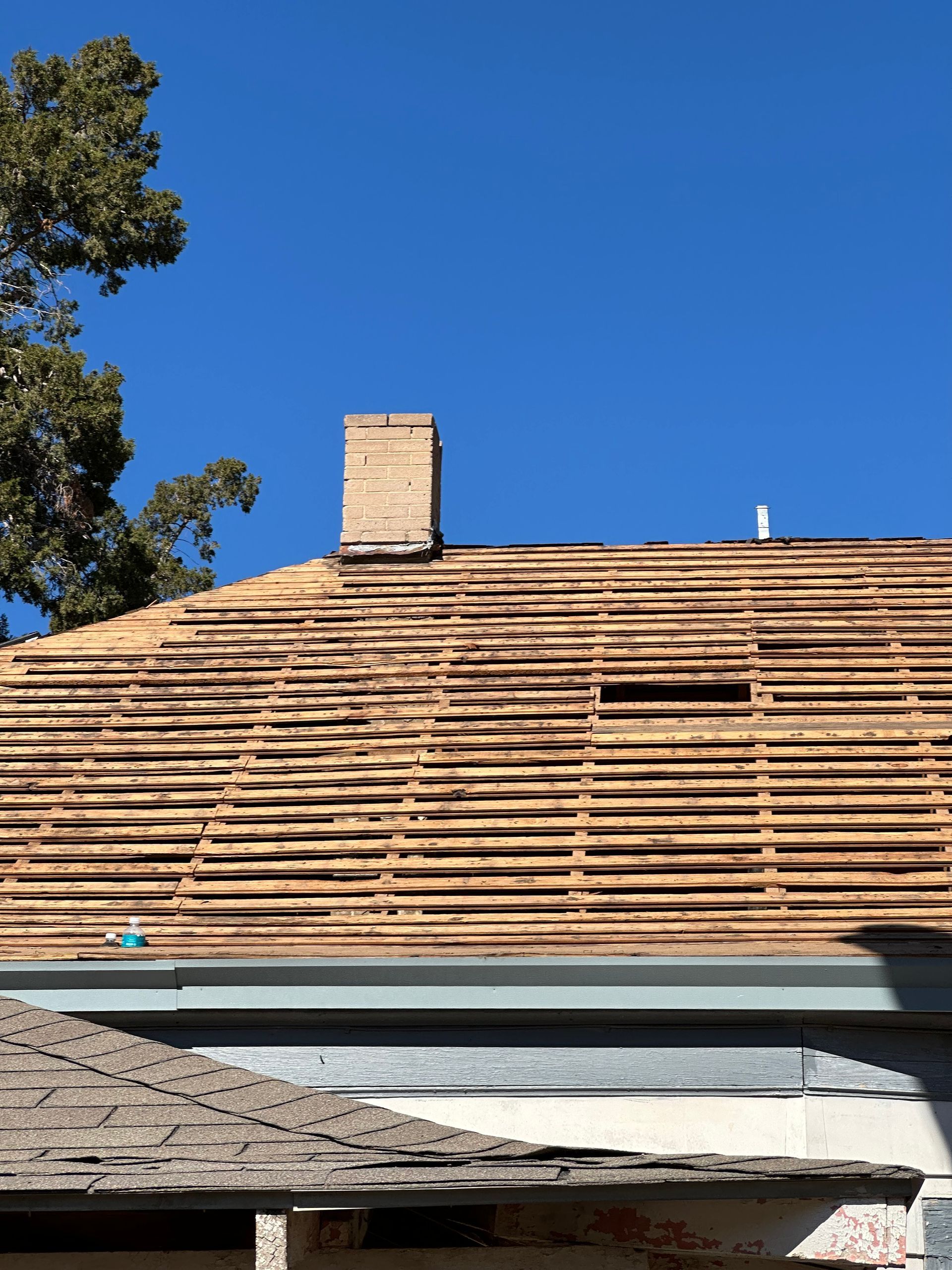 Roof being replaced; wooden framework exposed, brick chimney, blue sky background.