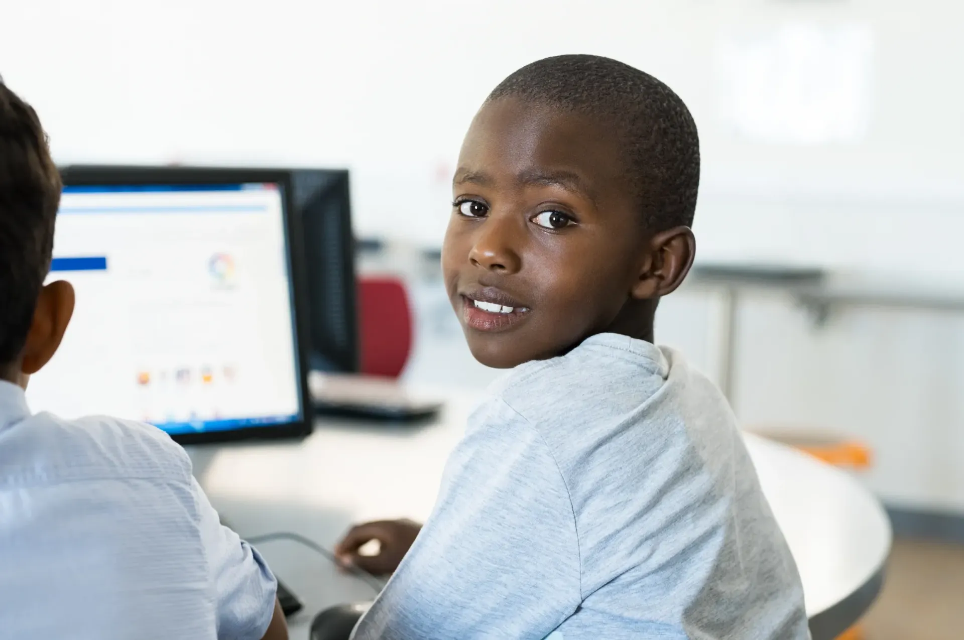 A young boy is sitting at a desk in front of a computer.
