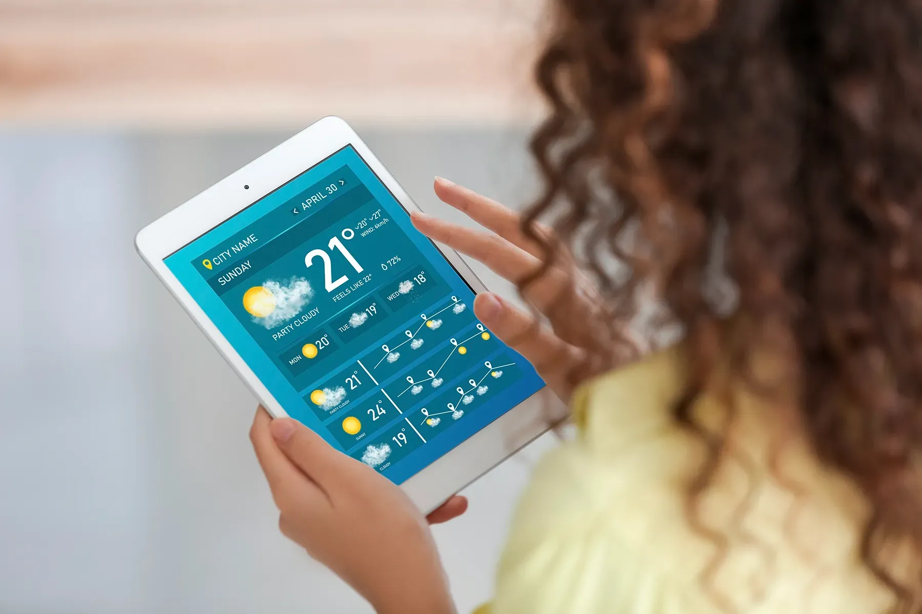 A woman is holding a tablet with the weather on it.