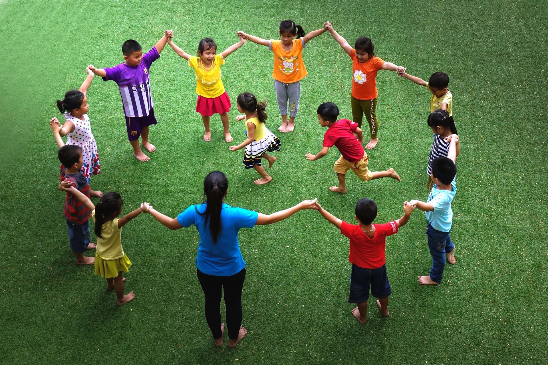 A group of children on the grass holding hands while two children run through.