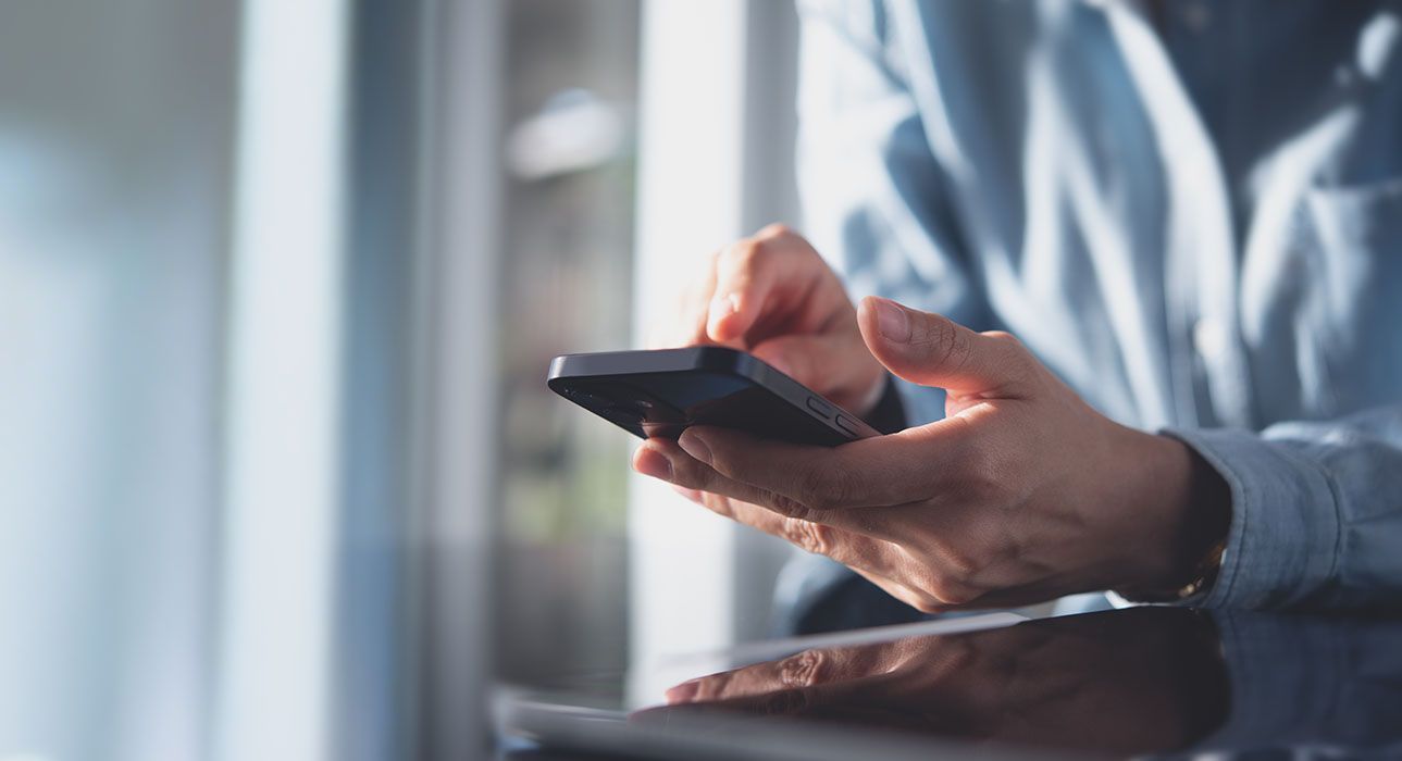 Person using a smartphone, blurred background with natural light. Hands hold the phone.