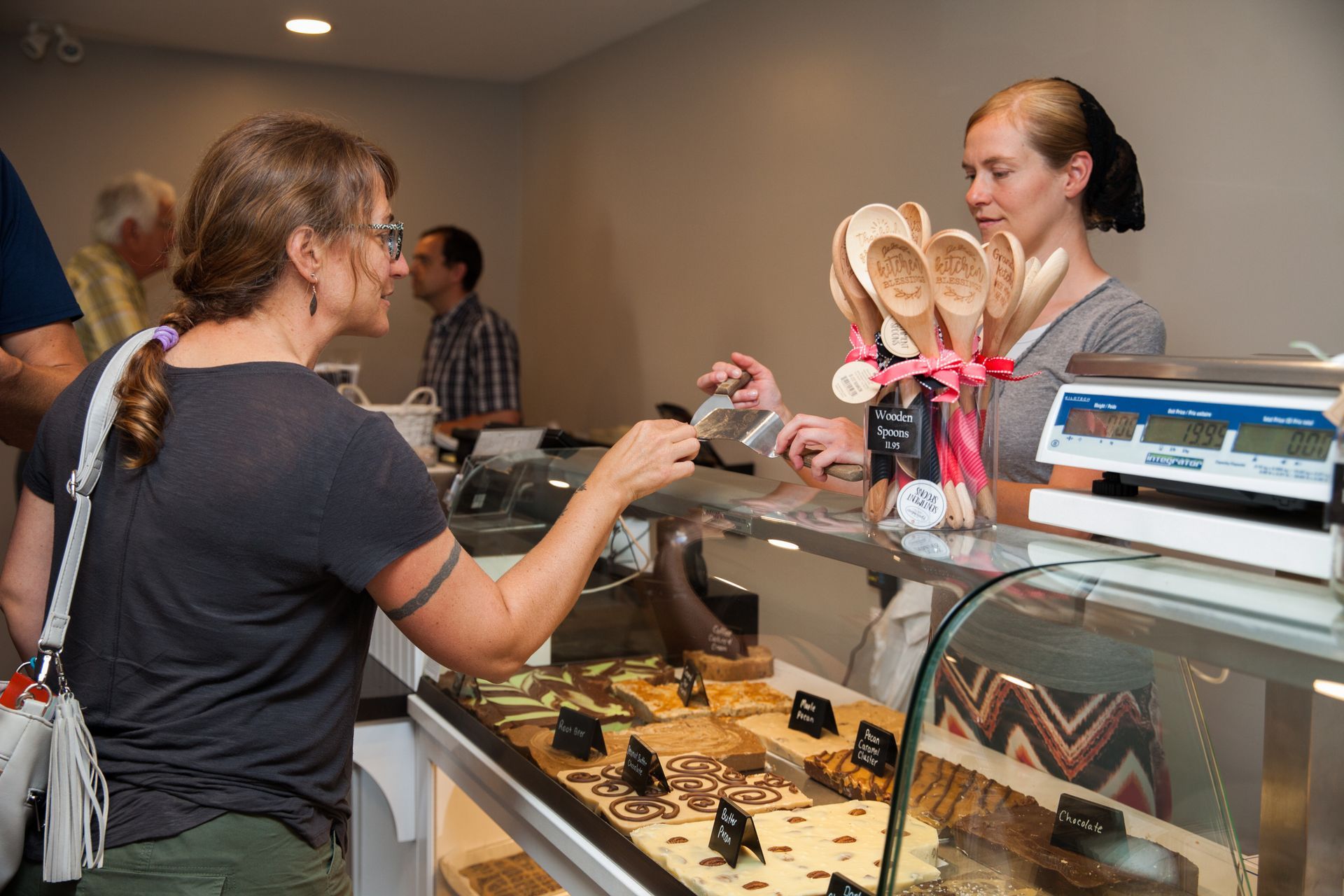 A woman is standing at a counter in a bakery talking to another woman.