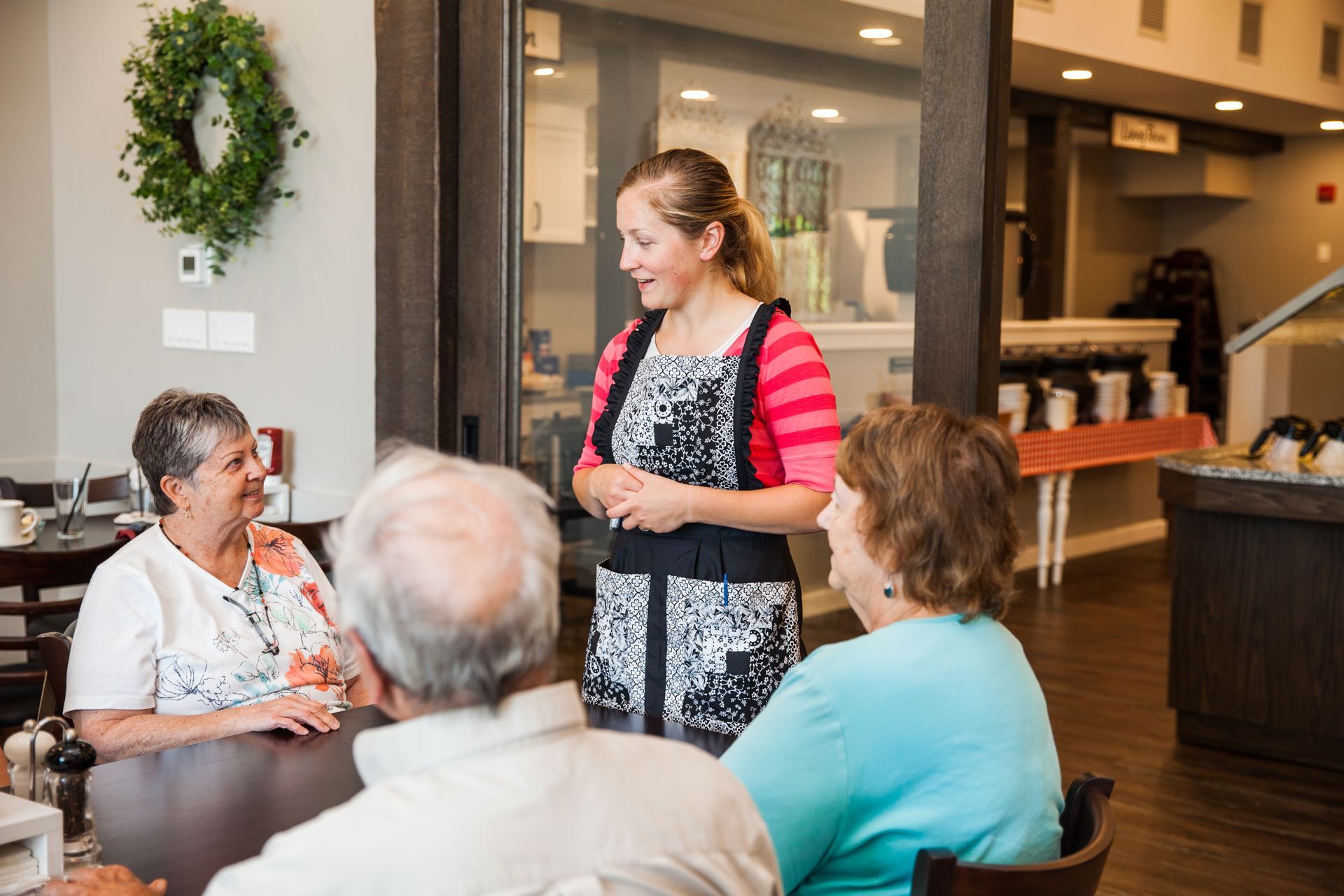A woman is talking to a group of people sitting at a table in a restaurant.