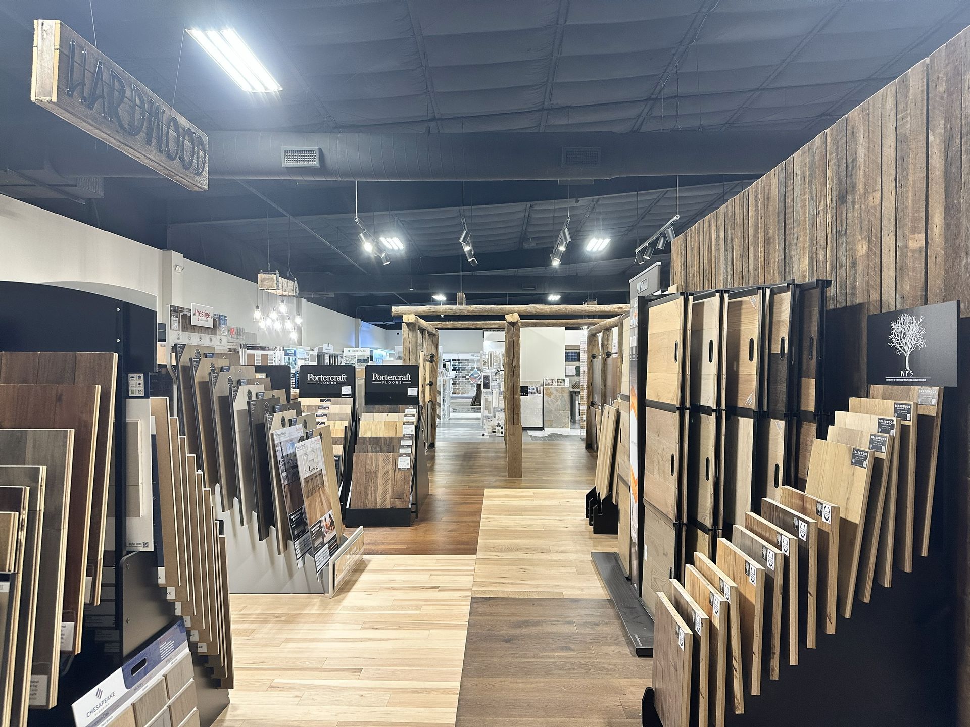 Interior view of a flooring showroom featuring rows of wooden planks and tile samples on display racks.