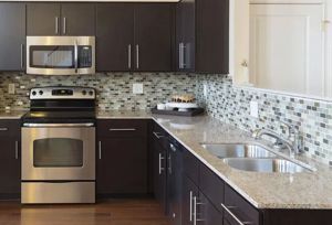A modern kitchen with dark brown cabinets, granite countertops, a stainless steel oven, and a tiled backsplash.