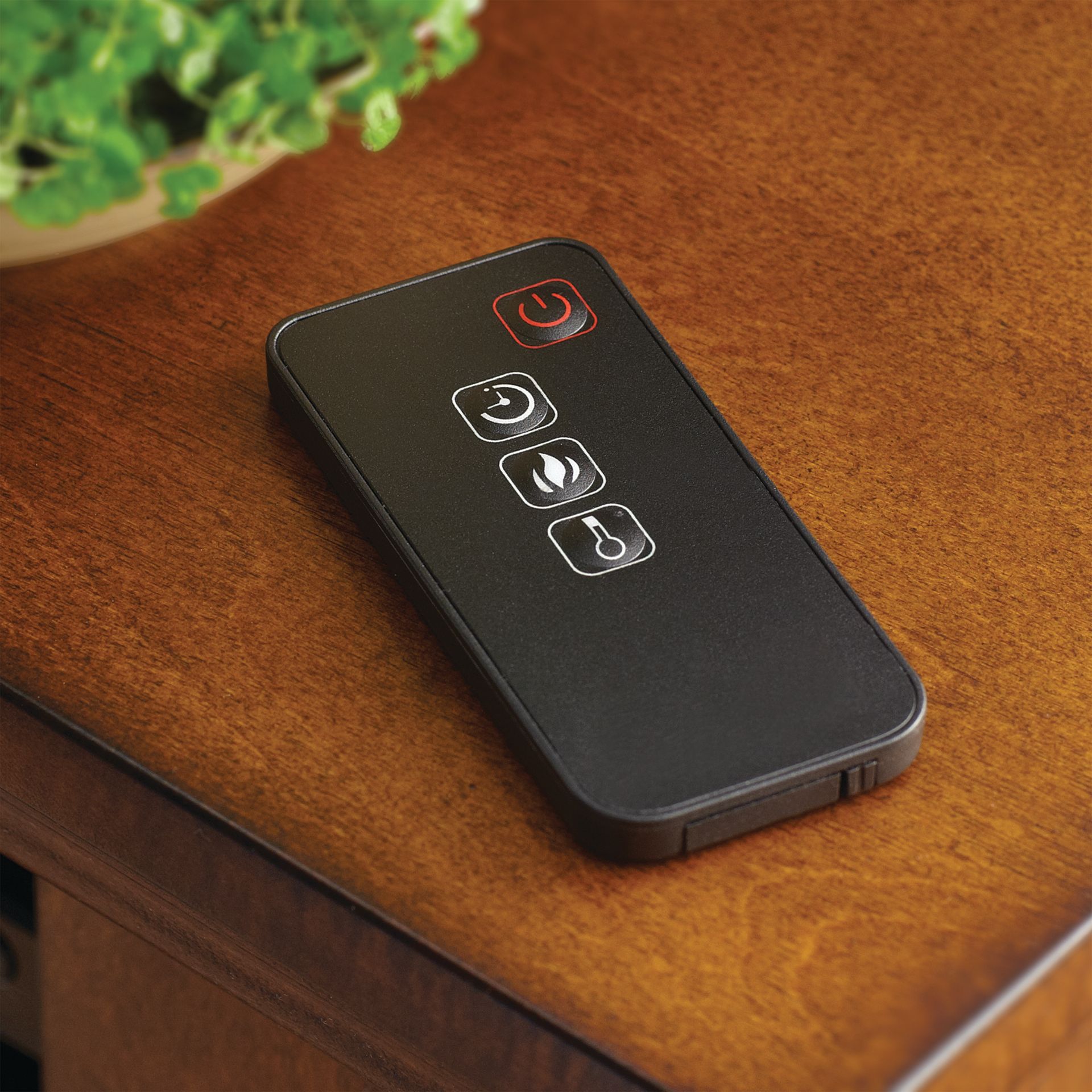 Black remote control on a wooden surface, with symbols for power, settings, and heat.