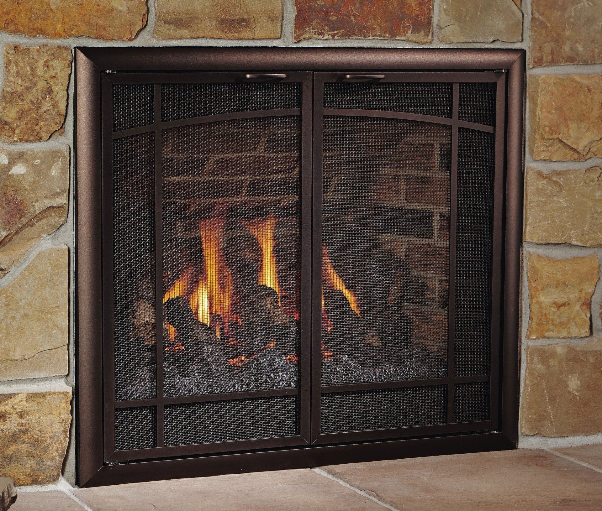 Fireplace with brown metal mesh screen and burning flames in a stone wall setting.