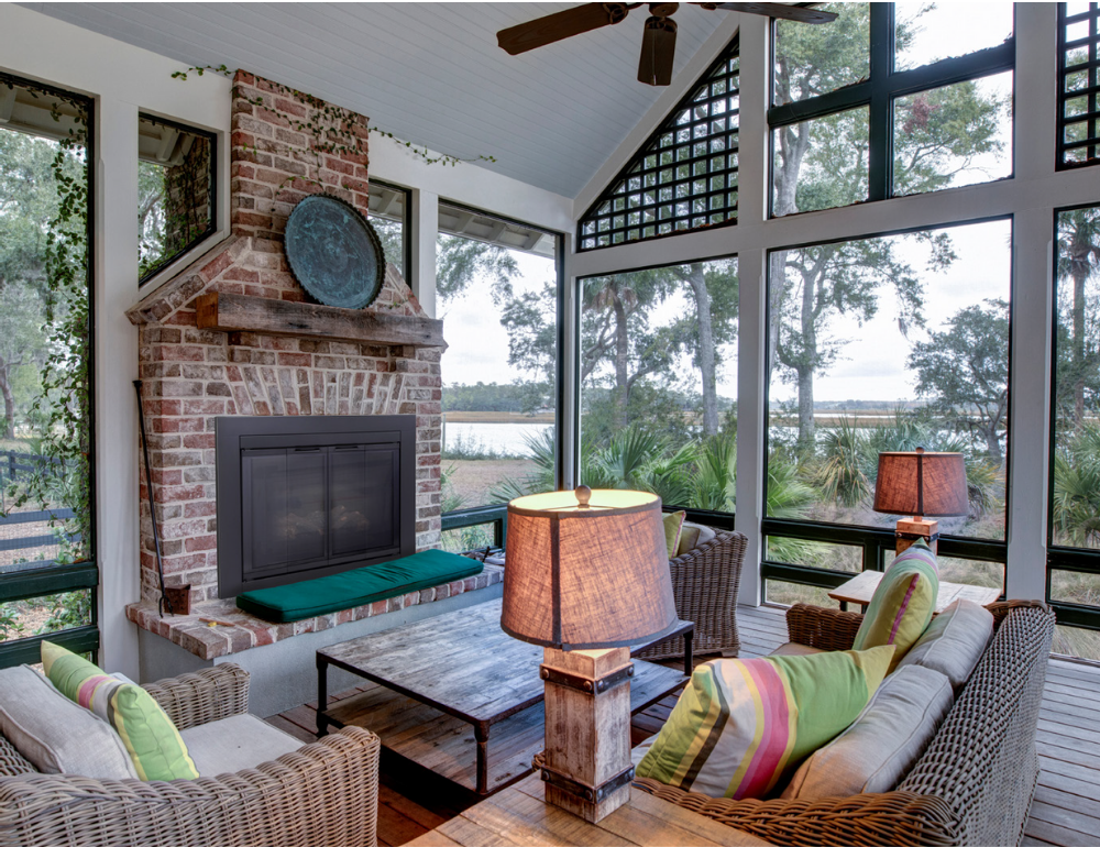 Sunroom with brick fireplace, wicker furniture, large windows, and outdoor view.