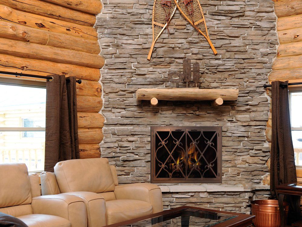 Stone fireplace with fire, log mantel and snowshoes in a rustic log cabin setting.