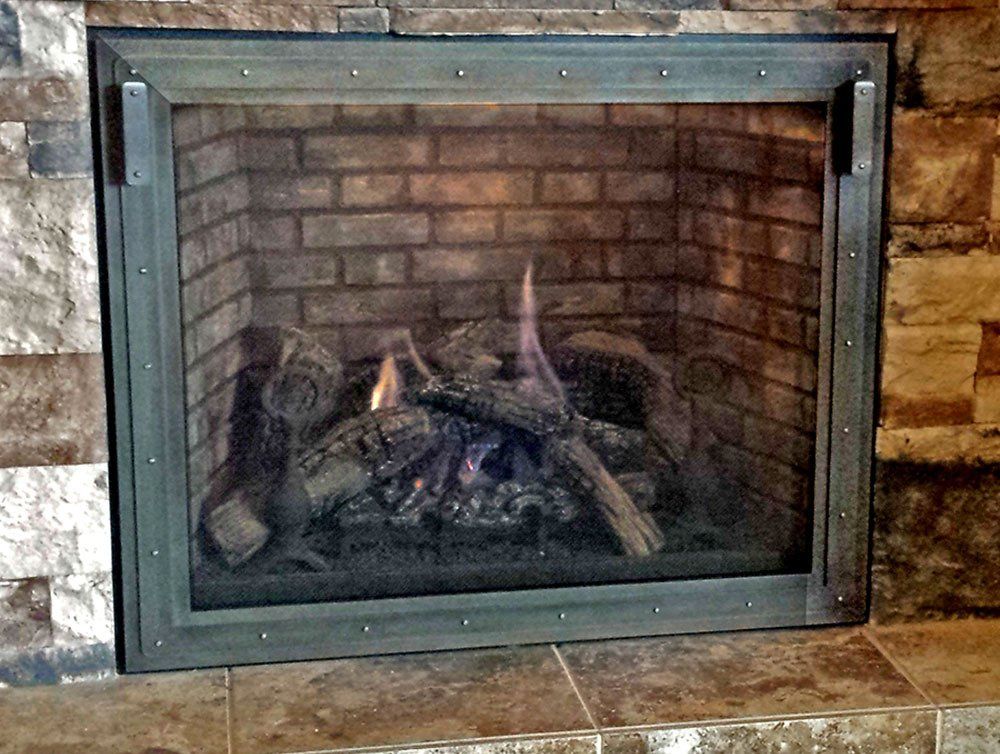 Fireplace with burning logs behind a glass screen in a brick enclosure.