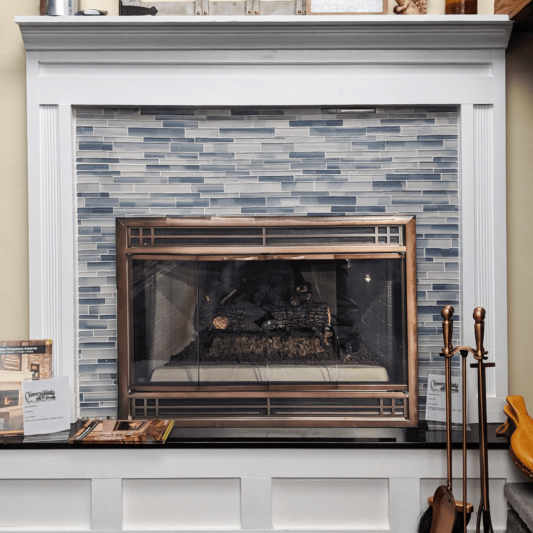 Fireplace with blue-gray tile surround and bronze fire screen, framed by white molding.