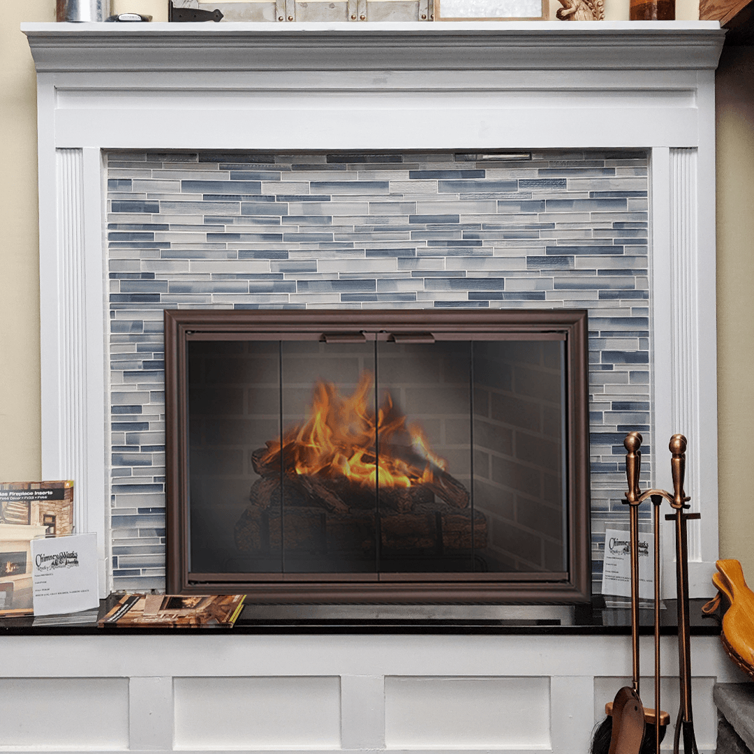 Fireplace with burning fire, glass screen, blue tile, white mantel, and fireplace tools.