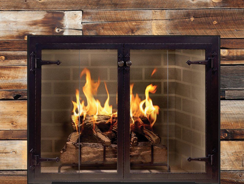 Fireplace with burning logs behind glass doors, set in a wood-paneled wall.