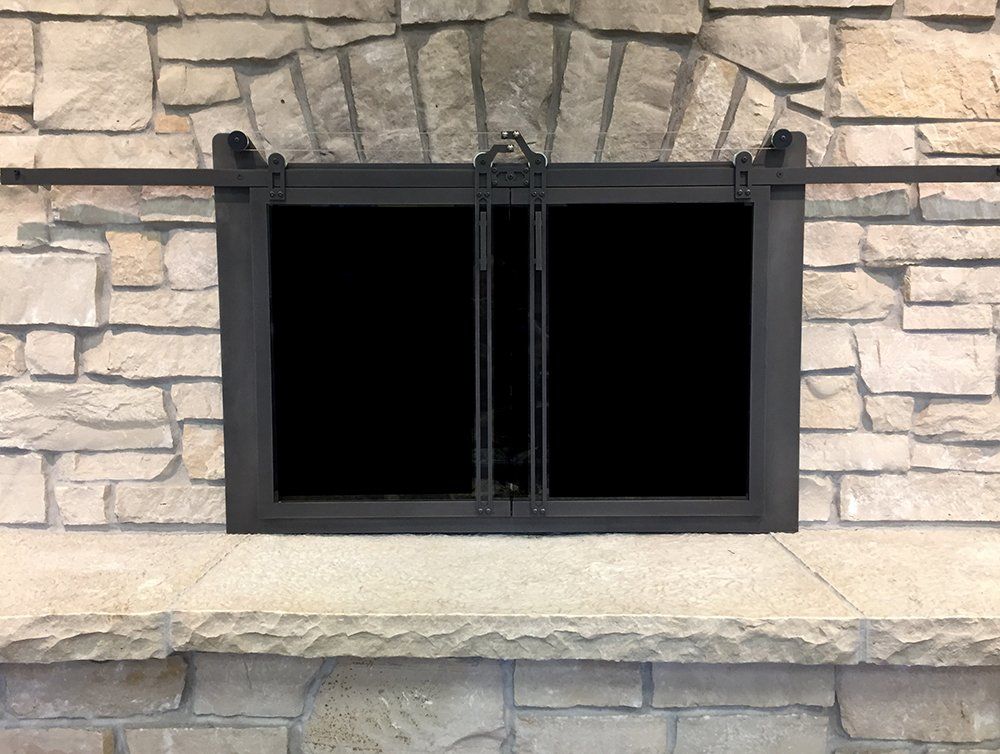 Black fireplace doors with a sliding mechanism against a stone fireplace.