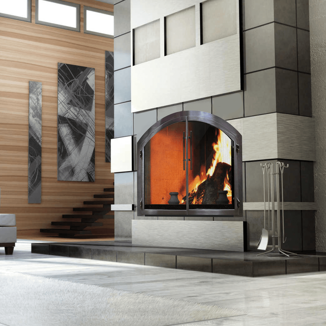 Fireplace with arched glass doors, flames, surrounded by gray stone and wooden walls; art and stairs in background.