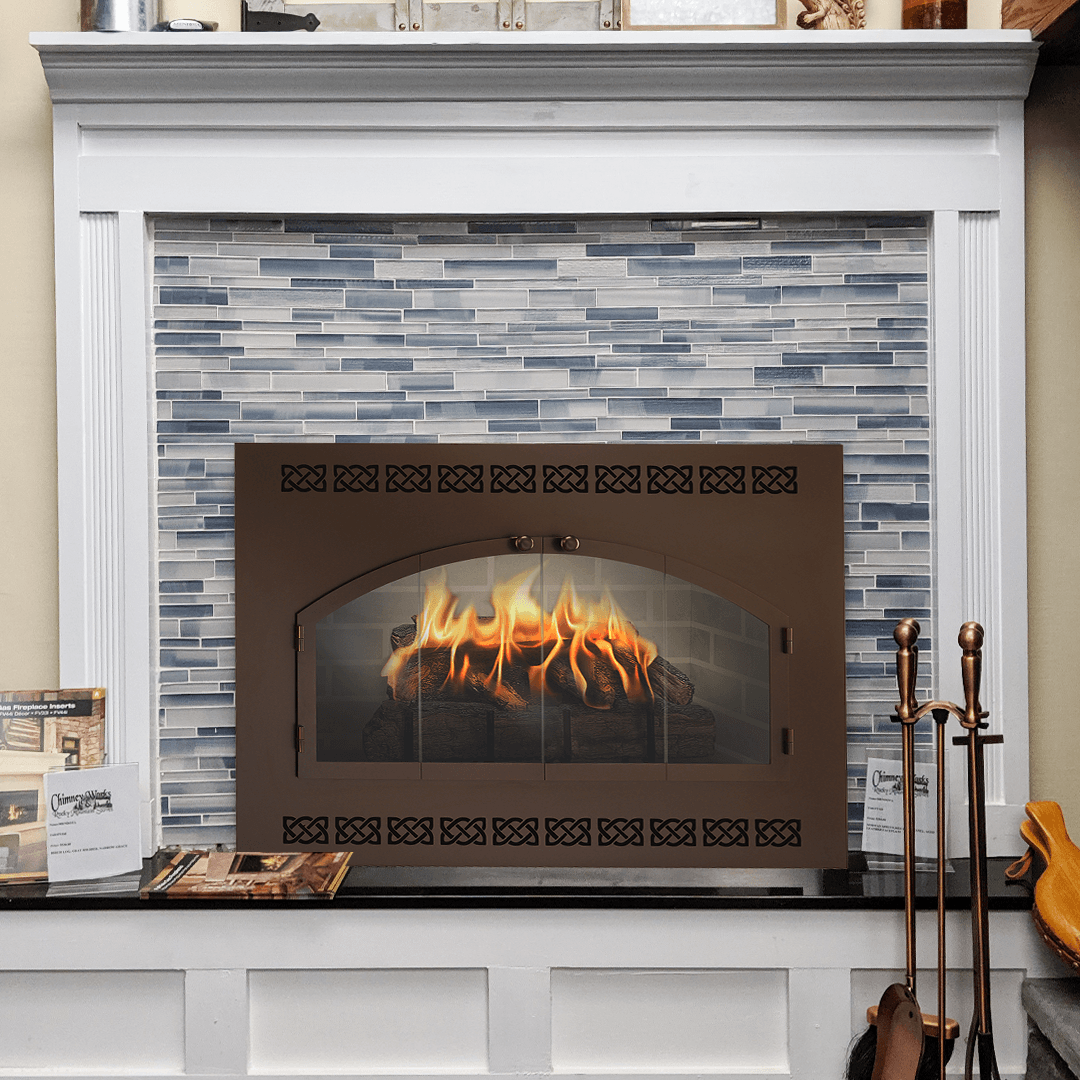 Fireplace with flames behind a bronze door, set in front of blue-gray tiled wall.
