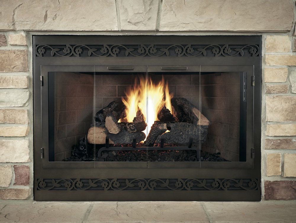 Fireplace with lit logs behind glass doors, set in a stone wall.