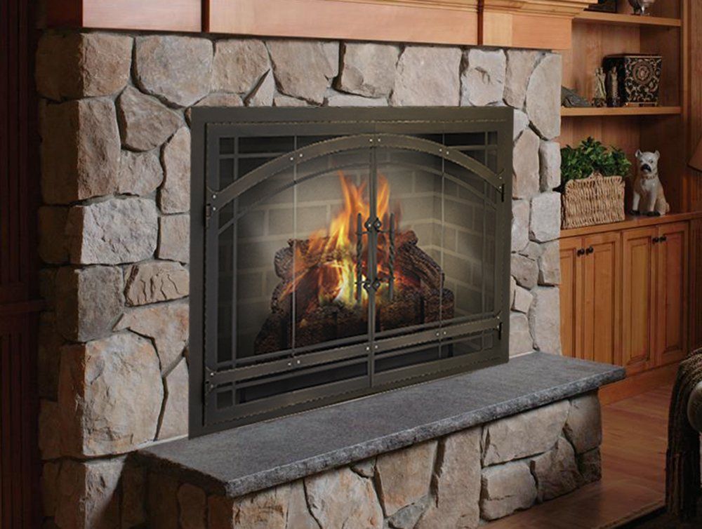 Fireplace with stone surround, metal screen, and burning logs.