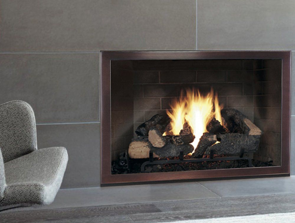 Fireplace with burning logs, inside a bronze-colored frame, set against gray tiled wall.