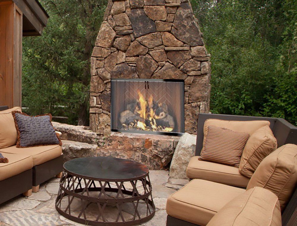 Outdoor stone fireplace with a fire, surrounded by seating on a patio.