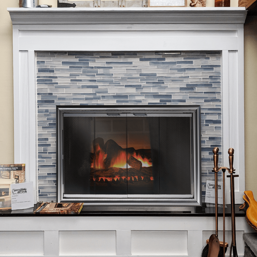 Fireplace with blue-tiled surround, white mantel, and burning fire. Black hearth with tools.